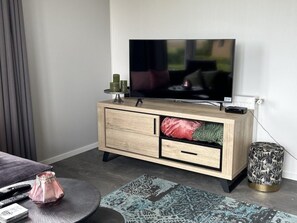 Ein modernes Wohnzimmer mit Flachbildfernseher, einer Holzkabine mit Schubladen, einem runden Beistelltisch mit Vase und einem gemusterten Teppich.