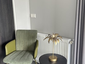 Ein Eckzimmer mit Heizkörper, einem Sessel und einem kleinen Tisch mit einer dekorativen Lampe.