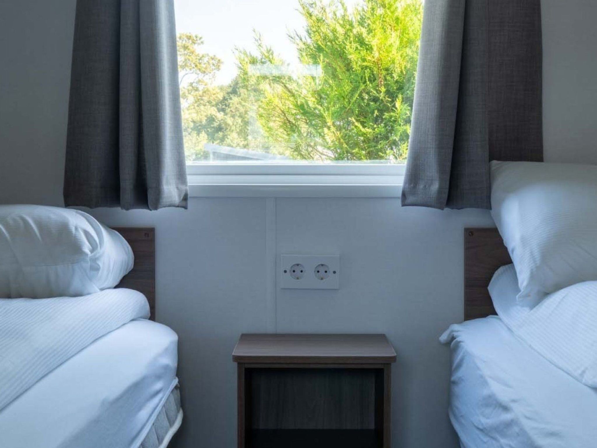 A bedroom with two single beds, a window with curtains, and a small bedside table.