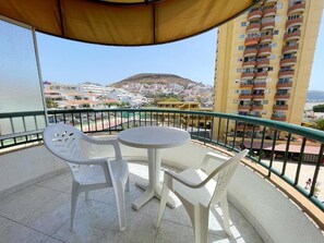 A balcony with a round table and two chairs, overlooking a residential area with a hill in the background. - Torres del Sol (Arona)