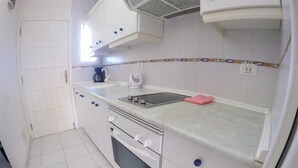 A compact kitchen with white cabinets, a built-in oven, a microwave, and a sink. - Torres del Sol (Arona)