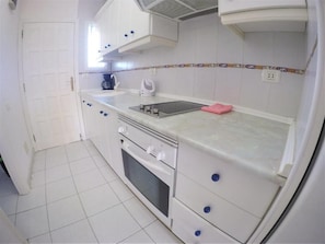 A compact kitchen with white cabinets, a built-in oven, a microwave, and a sink. - Torres del Sol (Arona)