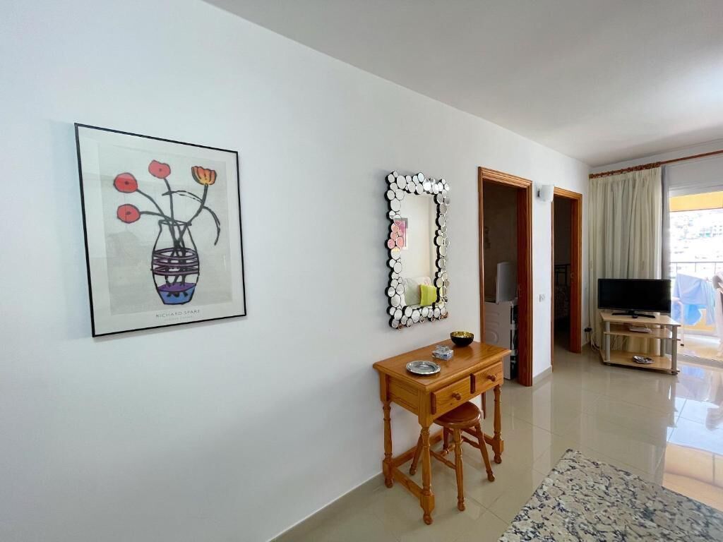 Une pièce comprenant un bureau, une œuvre d’art encadrée, un miroir décoratif, un téléviseur et une vue sur l’extérieur, visible à travers une porte.