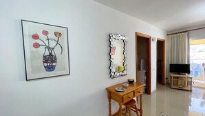 A room with a desk, a framed artwork, a decorative mirror, a television, and a view through a door. - Torres del Sol (Arona)