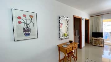 Une pièce comprenant un bureau, une œuvre d’art encadrée, un miroir décoratif, un téléviseur et une vue sur l’extérieur, visible à travers une porte.