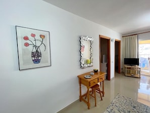 A room with a desk, a framed artwork, a decorative mirror, a television, and a view through a door. - Torres del Sol (Arona)