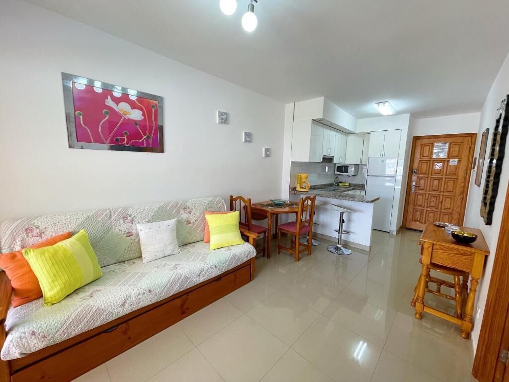 Una sala de estar con un sofá, una mesa de comedor y sillas. Cuenta con una zona de cocina con armarios y electrodomésticos.