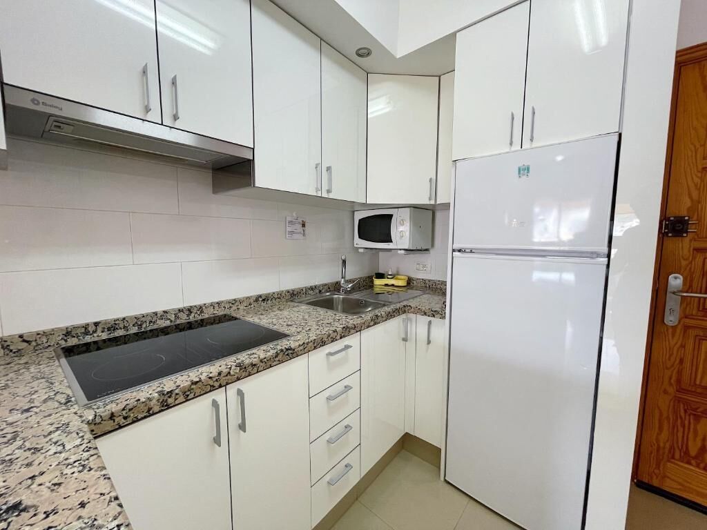 A kitchen with white cabinets, a granite countertop, a microwave, and a refrigerator.