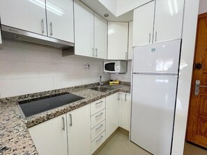 A kitchen with white cabinets, a granite countertop, a microwave, and a refrigerator. - Torres del Sol (Arona)