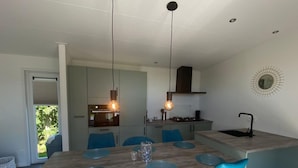 A modern kitchen with a central island, blue chairs, pendant lighting, and a view of the outdoors. - Vakantiepark de Zeeuwse Parel - de Schelde by Interhome (Scherpenisse)