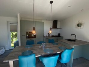 A modern kitchen with a central island, blue chairs, pendant lighting, and a view of the outdoors. - Vakantiepark de Zeeuwse Parel - de Schelde by Interhome (Scherpenisse)