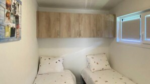 A small bedroom with two single beds, a wooden wardrobe, and a wall-mounted picture. - Vakantiepark de Zeeuwse Parel - de Schelde by Interhome (Scherpenisse)