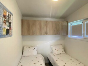 A small bedroom with two single beds, a wooden wardrobe, and a wall-mounted picture. - Vakantiepark de Zeeuwse Parel - de Schelde by Interhome (Scherpenisse)