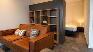 A modern living room with a brown leather sofa, a wooden bookshelf, and a bed with a nightstand. - De Witte Brugh- 't Fennoat by Interhome (Buren FR)