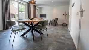 A modern dining area with a wooden table and chairs, a pendant light, and a television on the wall. - De Witte Brugh- 't Fennoat by Interhome (Buren FR)