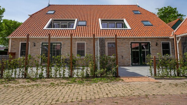 A two-story house with a red-tiled roof, a brick facade, and a fenced garden area. - De Witte Brugh- 't Fennoat by Interhome (Buren FR)