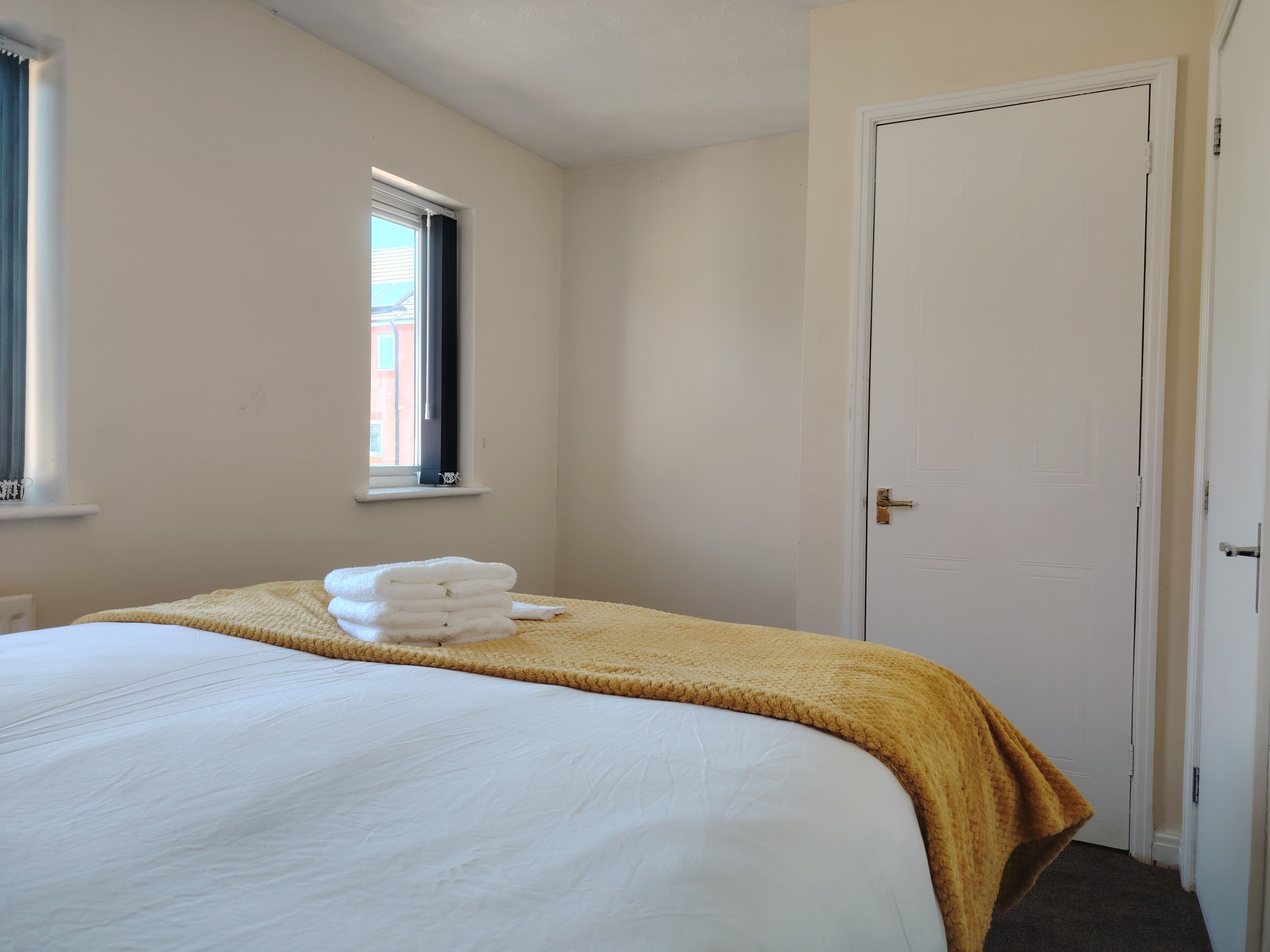 A hotel room with a bed, a window, a door, and a stack of white towels.