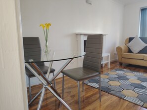 A modern living room with a glass dining table, two chairs, a sofa, and a patterned rug. - 2‑Bedroom Home in Walsall – Ideal Location for Work, Study & Travel (Walsall)