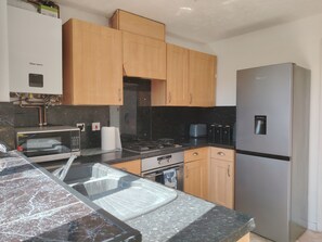 A modern kitchen with wooden cabinets, a stainless steel refrigerator, a microwave, and a gas stove. - 2‑Bedroom Home in Walsall – Ideal Location for Work, Study & Travel (Walsall)
