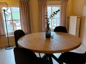 Una mesa redonda de madera con cuatro sillas negras, un florero con una planta y una lámpara de pie.