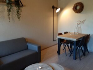 Ein Wohnzimmer mit Sofa, Esstisch mit Stühlen, Stehlampe und Wandkrans.