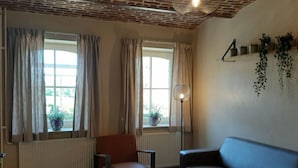 A living room with a brick ceiling, two windows with curtains, a radiator, a sofa, a chair, and a small table with candles. - Recreatieboerderij Tergracht - t Schob by Interhome (Epen)