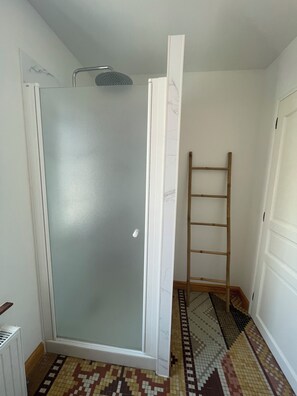 Ein Zimmer mit Duschkabine aus Glas, einer Holzleiter und einem gemusterten Boden.