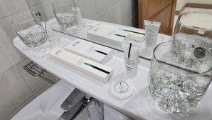 A bathroom counter with toiletries, a glass of water, and a glass of alcohol.