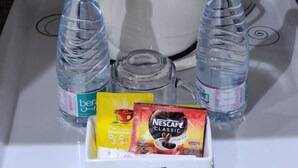 A white kettle, two water bottles, a glass, and a Nescafe Classic coffee packet on a white tray.