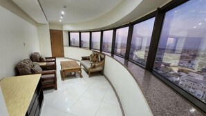 A curved room with a high ceiling, a seating area with a sofa and a table, and large windows offering a city view.