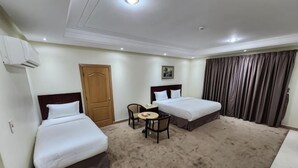 A hotel room with two beds, a small table, a chair, and a door.