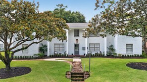 A white building with a central entrance, surrounded by a well-maintained lawn and trees.