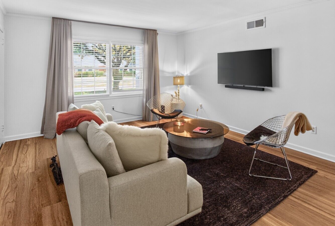 Ein modernes Wohnzimmer mit einer Couch, einem Couchtisch, einem Fernseher und einem Fenster mit Vorhängen.