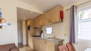 Cocina compacta con muebles de madera, un microondas y una estufa a gas. Hay una ventana con cortina a rayas y una puerta que da a otra habitación.
