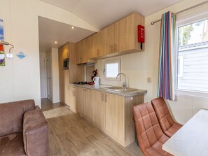 A compact kitchen with wooden cabinets, a microwave, and a gas stove. There is a window with a striped curtain and a door leading to another room. - Camping de Molenhof - Lodge 4 personen by Interhome (Reutum)