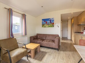 A living room with a brown sofa, a wooden coffee table, and a striped curtain. - Camping de Molenhof - Lodge 4 personen by Interhome (Reutum)