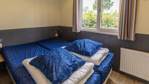 Habitación con dos camas, ventana con cortinas, radiador y un interruptor de luz en la pared.