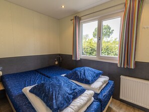 A room with two beds, a window with curtains, a radiator, and a wall-mounted light switch. - Camping de Molenhof - Lodge 4 personen by Interhome (Reutum)