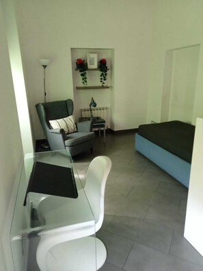 Ein kompakter Wohnraum mit Glastisch, grauem Sofa, blauem Bett und Heizkörper.
