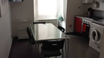 Een kleine keuken met een eettafel, stoelen, een wasmachine en een fornuis.