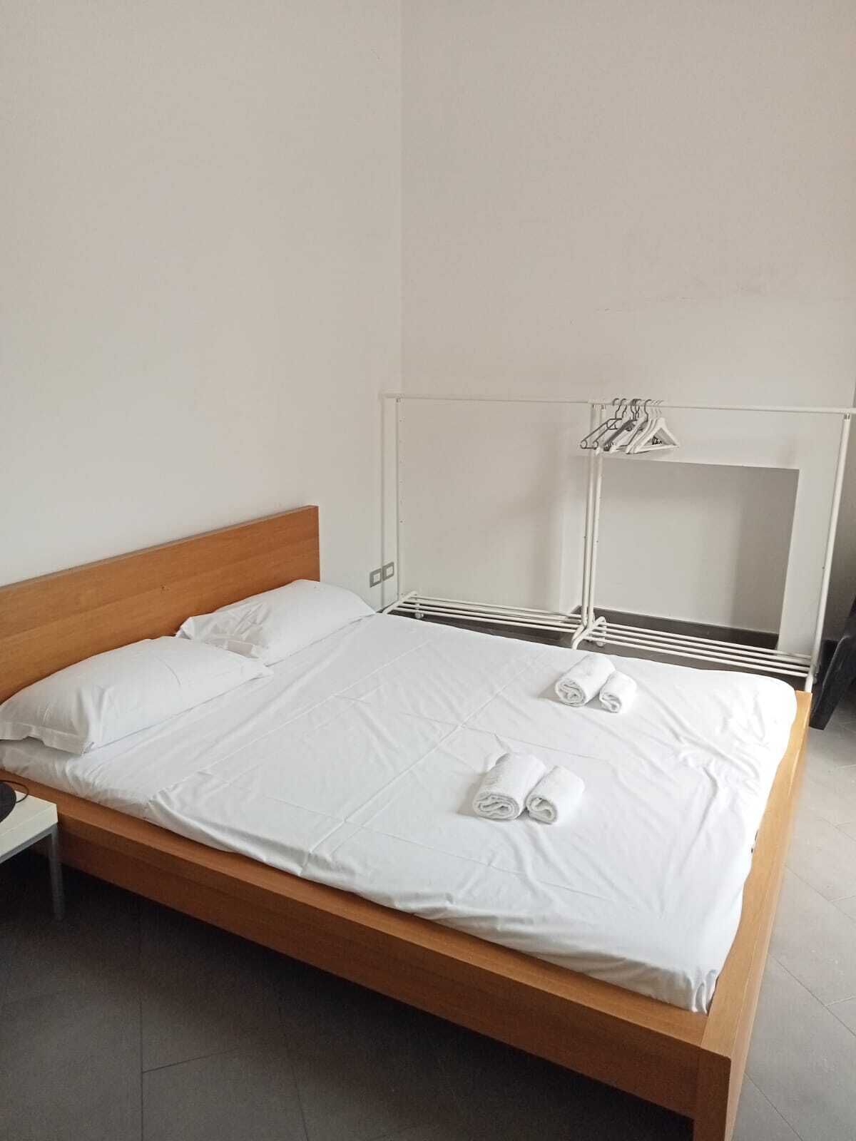 A bed with white linens and rolled towels, a wooden headboard, and a white wardrobe with a mirror.