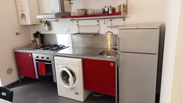 Una cucina compatta con piano cottura a gas, lavatrice integrata, frigorifero e lavello.