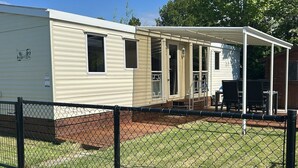 A mobile home with a covered patio area, a fenced yard, and a small table and chairs. - Beach Resort Kamperland - 1123 by Interhome (Kamperland)