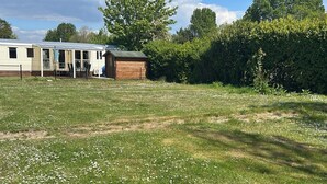 A grassy outdoor area with a wooden structure and a mobile home in the background. - Beach Resort Kamperland - 1123 by Interhome (Kamperland)