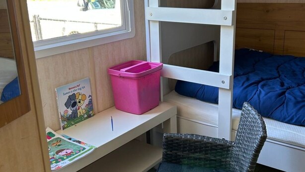A bunk bed with a pink storage box, a wicker chair, and a window with a view of a parked car and greenery. - Beach Resort Kamperland - 1123 by Interhome (Kamperland)