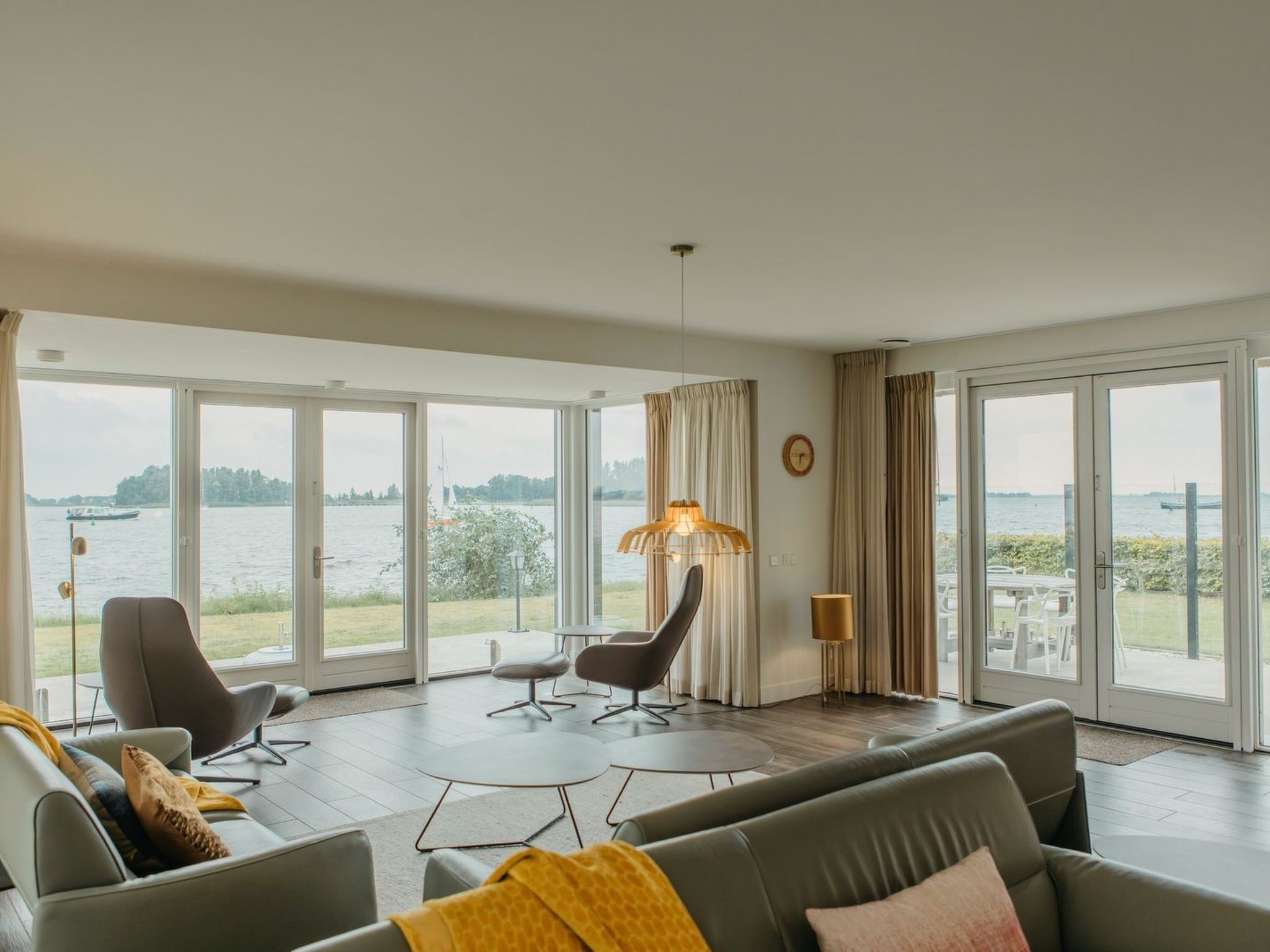 Amplia sala de estar con vista a un cuerpo de agua, ventanas grandes y muebles modernos.