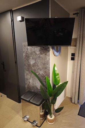 A modern living room with a flat-screen TV mounted on a wall, a potted plant, and a bench. - Beach Resort Kamperland - 622 by Interhome (Kamperland)