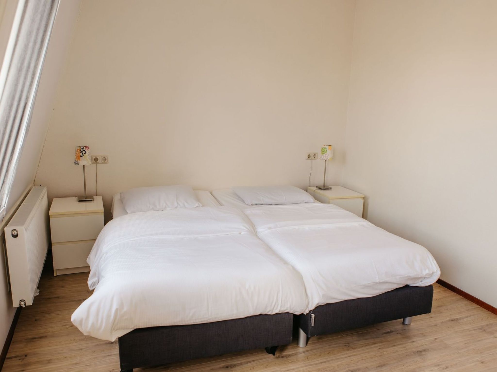 Un dormitorio con una cama doble, dos mesitas de noche, un radiador y una lámpara a cada lado.
