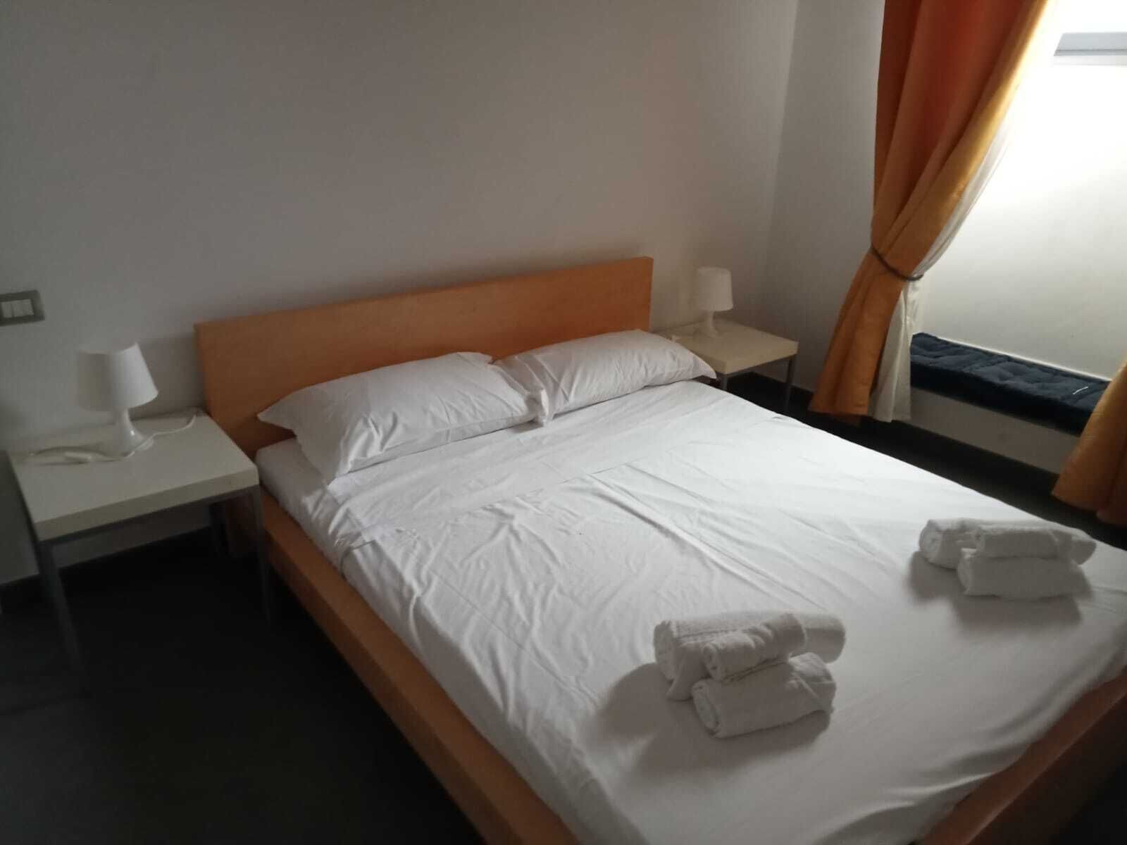 Ein Hotelzimmer mit einem Bett, einem Nachttisch mit Lampe und einem Fenster mit Vorhängen.