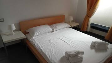 Ein Hotelzimmer mit einem Bett, einem Nachttisch mit Lampe und einem Fenster mit Vorhängen.